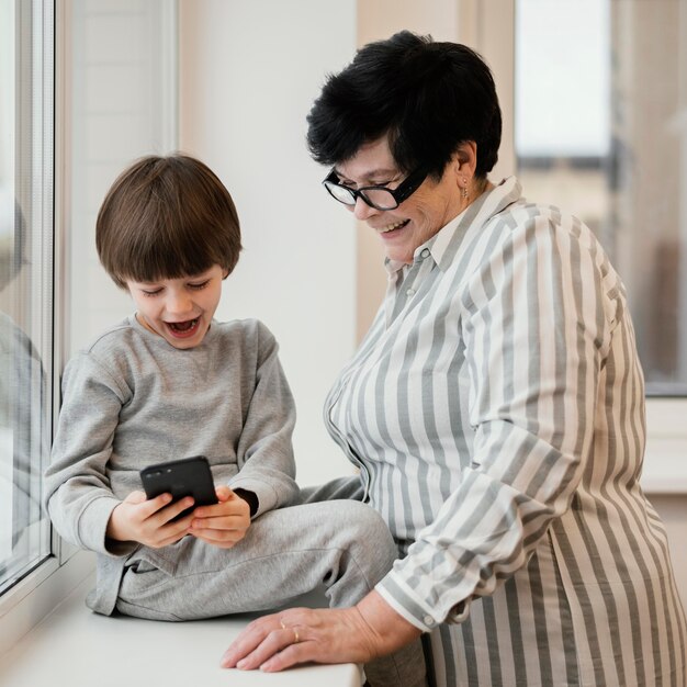 Smiley grootmoeder kijken kleinzoon spelen met smartphone