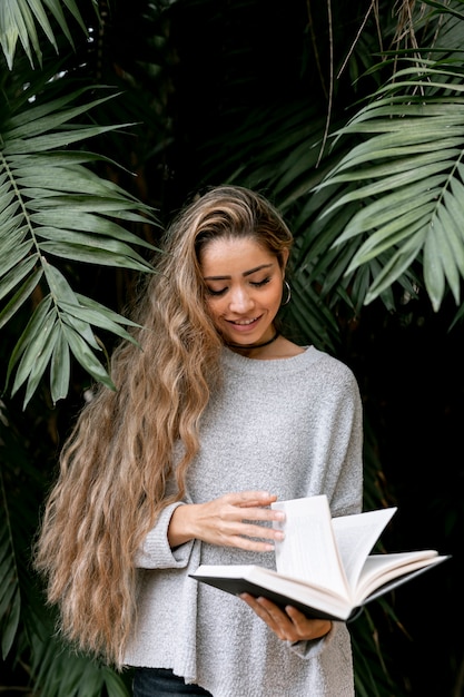 Gratis foto smiley jonge vrouw die een boek buiten leest