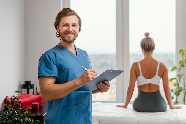 Smiley mannelijke osteopathische therapeut met klembord en vrouwelijke patiënt bij de kliniek