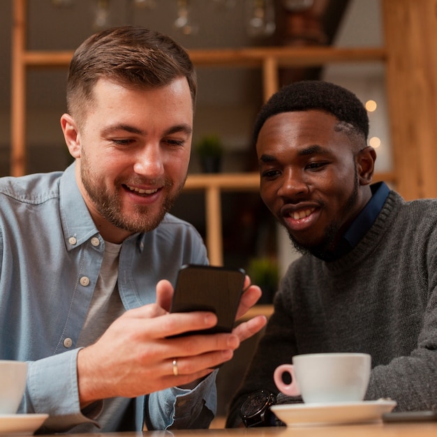 Smiley mannelijke vrienden die op mobiel kijken