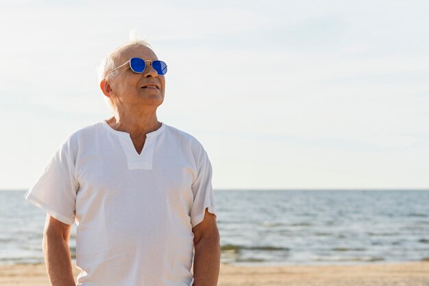 Smiley oudere man met zonnebril genieten van zijn tijd op het strand