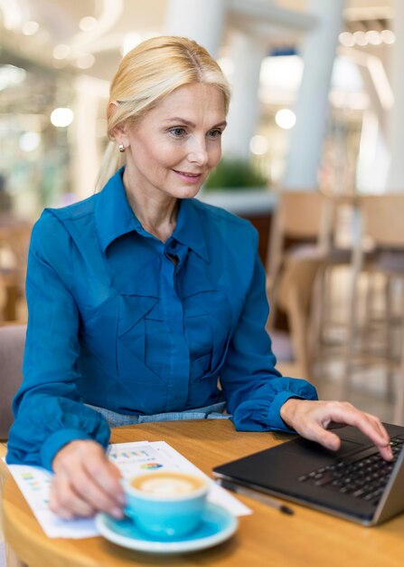 Smiley oudere zakenvrouw die op laptop werkt en koffie heeft