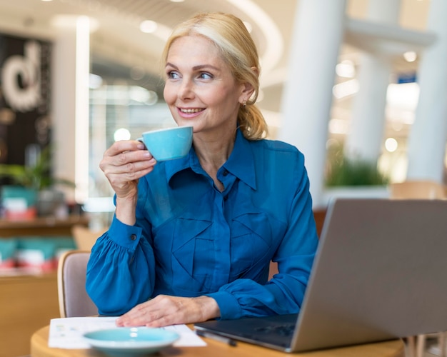Smiley oudere zakenvrouw genieten van een kopje koffie tijdens het werken