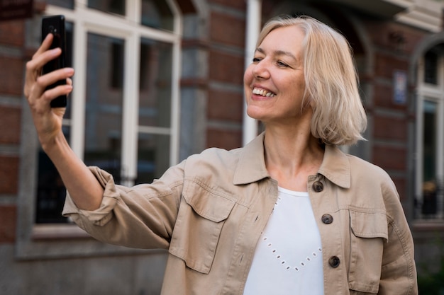 Gratis foto smiley senior vrouw die een selfie terwijl uit in de stad