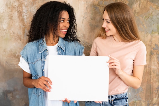 Gratis foto smiley-vriendinnen die leeg aanplakbiljet houden