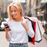 Gratis foto smiley vrouw boodschappentassen te houden en smartphone te kijken