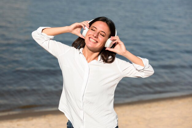 Smiley vrouw luisteren naar muziek op een koptelefoon op het strand