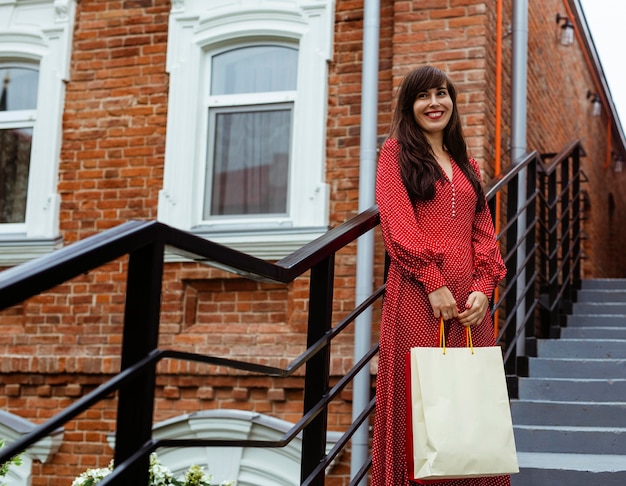 Gratis foto smiley vrouw poseren buitenshuis met boodschappentassen