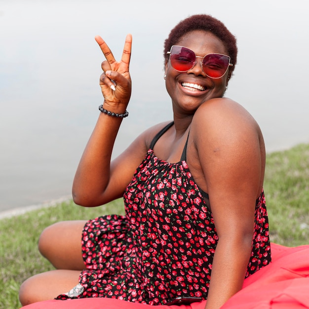 Smiley vrouw poseren buitenshuis op zitzak en vredesteken maken