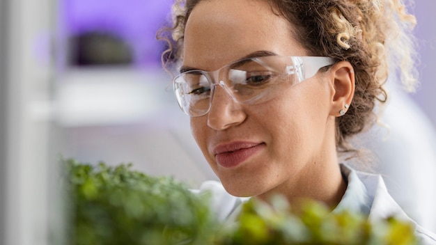 Smiley vrouwelijke onderzoeker in het laboratorium met veiligheidsbril en plant
