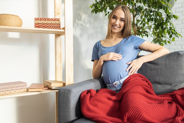 Gratis foto smiley zwangere zakenvrouw zittend op de bank en houdt haar buik