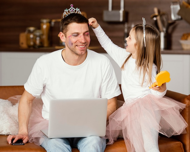 Gratis foto smileydochter die met vader speelt terwijl hij aan laptop werkt