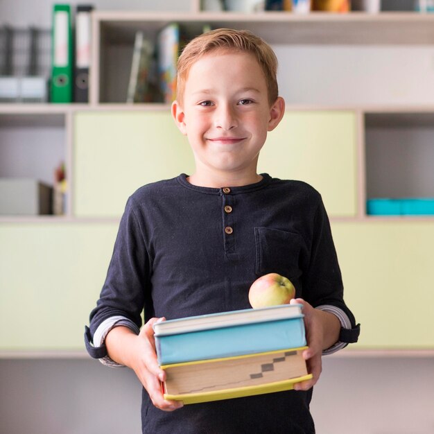 Smileyjongen die een heleboel boeken houdt