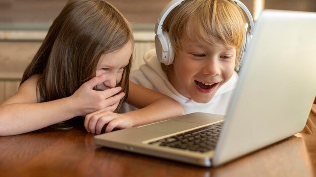 Smileykinderen die laptop en hoofdtelefoons samen gebruiken