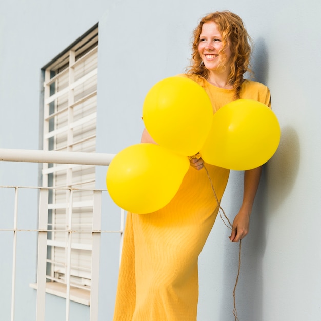 Gratis foto smileyvrouw die gele ballons houden