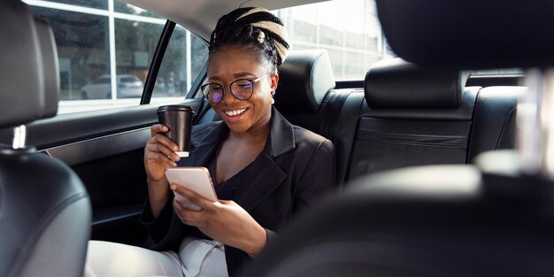 Smileyvrouw die koffie heeft en smartphone vanuit haar auto bekijkt