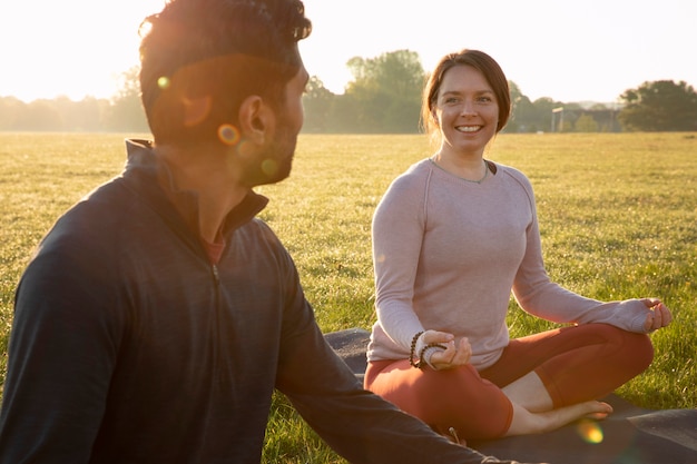 Gratis foto smileyvrouw en man die buiten op yogamat mediteren