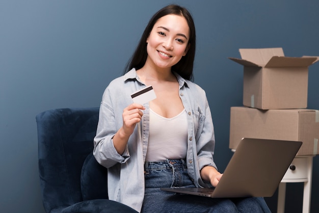 Smileyvrouw het stellen met creditcard en laptop naast dozen