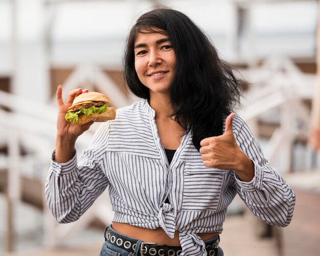 Smileyvrouw met hamburger die goedkeuring toont