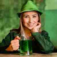 Gratis foto smileyvrouw met hoed die st. patrick's day aan de bar met een drankje