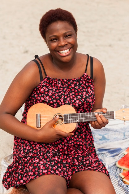 Gratis foto smileyvrouw op strand met gitaar