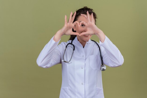 Smilinng arts jong meisje medische jurk dragen stethoscoop dragen toont hart gebaar op groene achtergrond