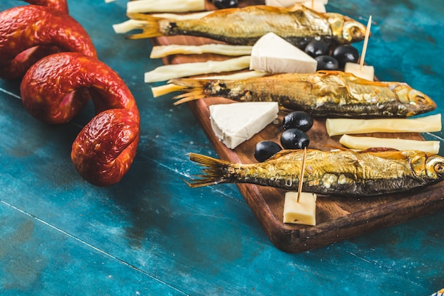 Gratis foto snack bord met plakjes worst, kaasblokjes en zwarte olijven met crackers en droge vis op de blauwe tafel