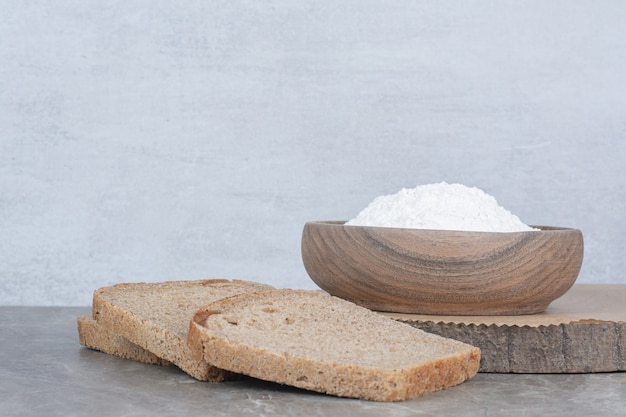 Sneetjes bruin brood met bloem op marmeren oppervlak