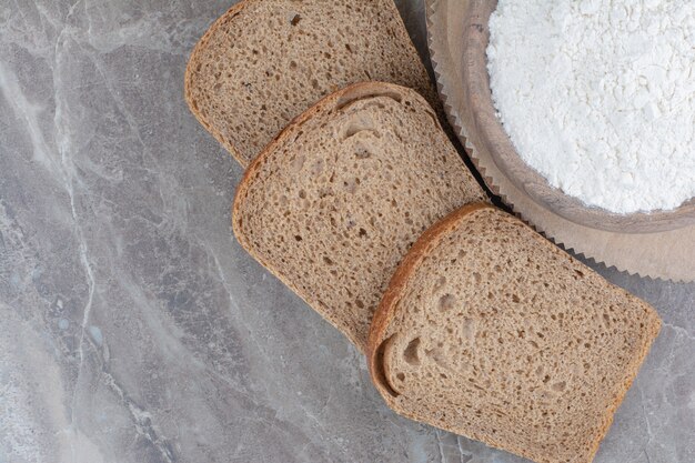 Sneetjes bruin brood met bloem op marmeren oppervlak