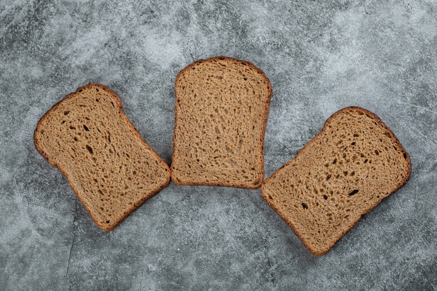 Gratis foto sneetjes bruin vers brood op een grijze ondergrond.