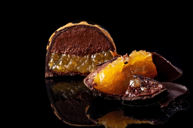 Gratis foto snijd luxe handgemaakte snoepjes met chocolade en gele confiture vulling op zwarte achtergrond. exclusieve handgemaakte bonbon