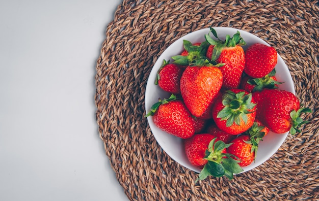 Sommige aardbeien in een kom op onderzetter en witte achtergrond, hoogste mening.