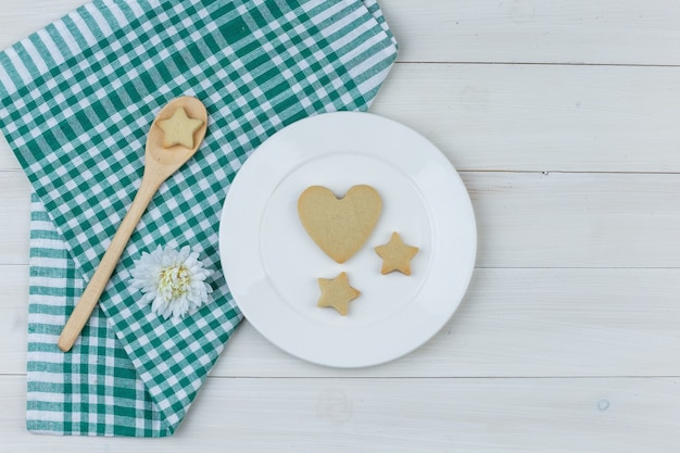 Sommige koekjes met bloem in plaat en houten lepel op houten en vlakke keukenhanddoekachtergrond, leggen.