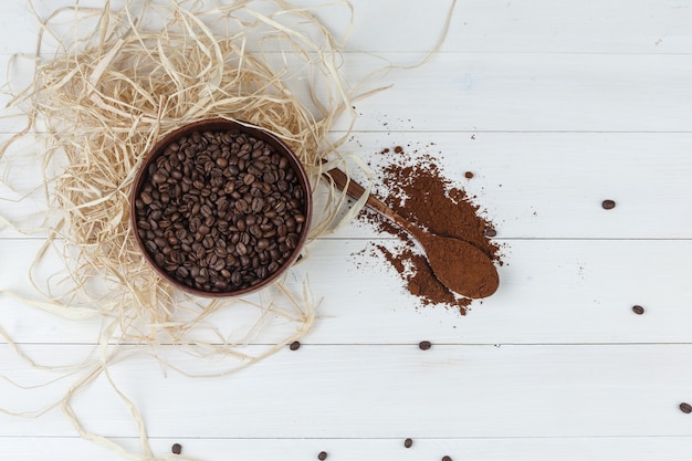 Sommige koffiebonen met gemalen koffie in een kom op houten achtergrond, bovenaanzicht.