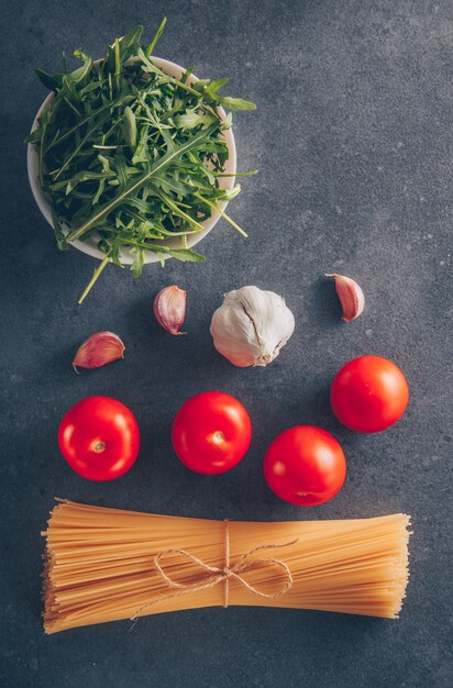 Sommige spaghettideegwaren met Groenen, tomaten en knoflook op grijze geweven achtergrond, hoogste mening.