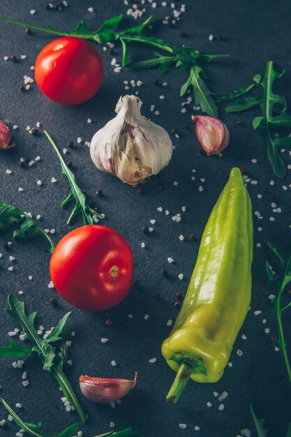 Sommige tomaten met knoflook, Groenen en peper op grijze gestructureerde achtergrond, bovenaanzicht.