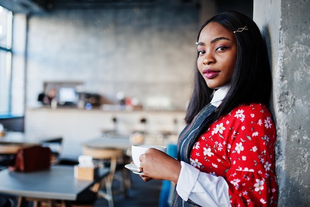 Sonfident jonge Afro-Amerikaanse vrouw in slimme vrijetijdskleding in café met een kopje warme drank in de hand