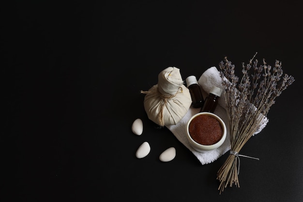 Spa-samenstelling met natuurlijke scrub, kruidenmassagezak, oliën en lavendel op een zwarte achtergrond, kopieerruimte.