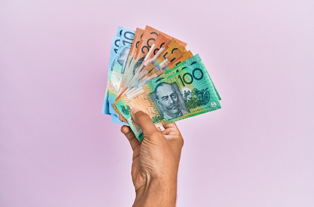 Gratis foto spaanse hand die australische dollarsbankbiljetten over geïsoleerde roze achtergrond houdt.