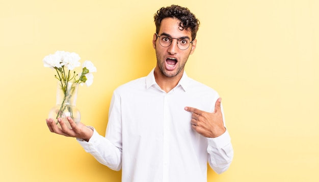 Spaanse knappe man die geschokt en verrast kijkt met wijd open mond, wijzend naar zichzelf. bloemen pot concept