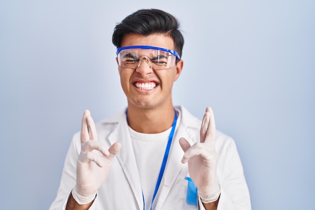 Gratis foto spaanse man aan het werk als wetenschapper gebarende vinger gekruist glimlachend met hoop en ogen gesloten geluk en bijgelovig concept