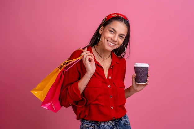 Spaanse mooie vrouw in rood shirt glimlachend bedrijf boodschappentassen op roze studio achtergrond geïsoleerd korting verkoop zwarte vrijdag houden