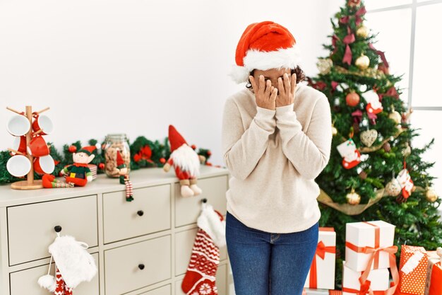 Spaanse vrouw van middelbare leeftijd die bij de kerstboom staat met een droevige uitdrukking die haar gezicht bedekt met handen terwijl ze huilt. depressie concept.