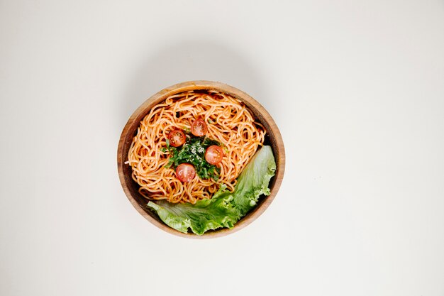 Spaghetti in tomatensaus met sla in een houten kom.