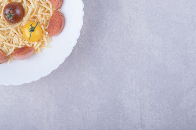 Spaghetti met geroosterde worstjes en tomaten in witte kom.