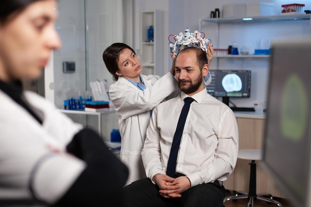 Specialist neuroloog vrouw aanpassen eeg headset analyseren hersenactiviteit van man patiënt monitoring zenuwstelsel informatie in medisch laboratorium. arts arts doet neurologie experiment