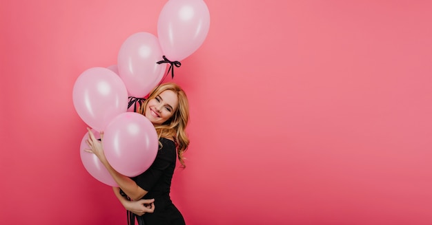 Spectaculair mooi meisje poseren met roze ballonnen en glimlachen. vrolijke blonde vrouw geïsoleerd op een lichte muur.