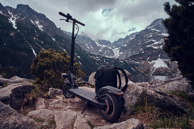 Spectaculair uitzicht op bergen, dennen en lage sombere wolken met rugzak en scooter aan de voorkant.