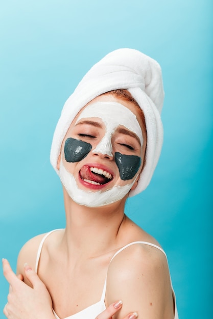 Spectaculaire vrouw die lol heeft tijdens huidverzorgingsbehandeling. studio shot van aantrekkelijk meisje met gezichtsmasker poseren op blauwe achtergrond.