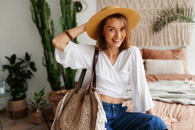 Speelse bohemien vrouw poseren in stijlvolle slaapkamer met een prachtig interieur, palmen en macrame